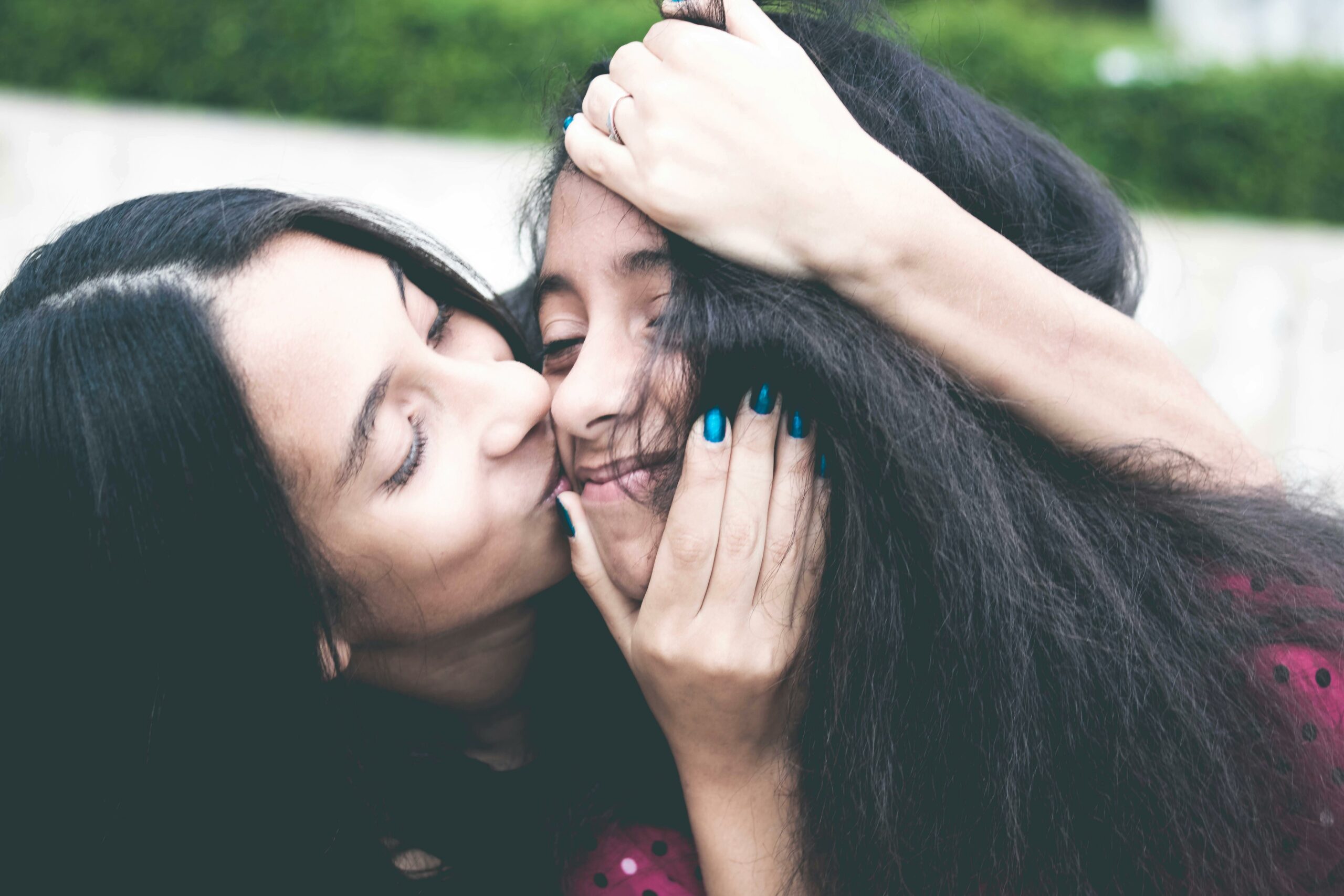 Mother kissing daughter on cheek while hugging head tightly.